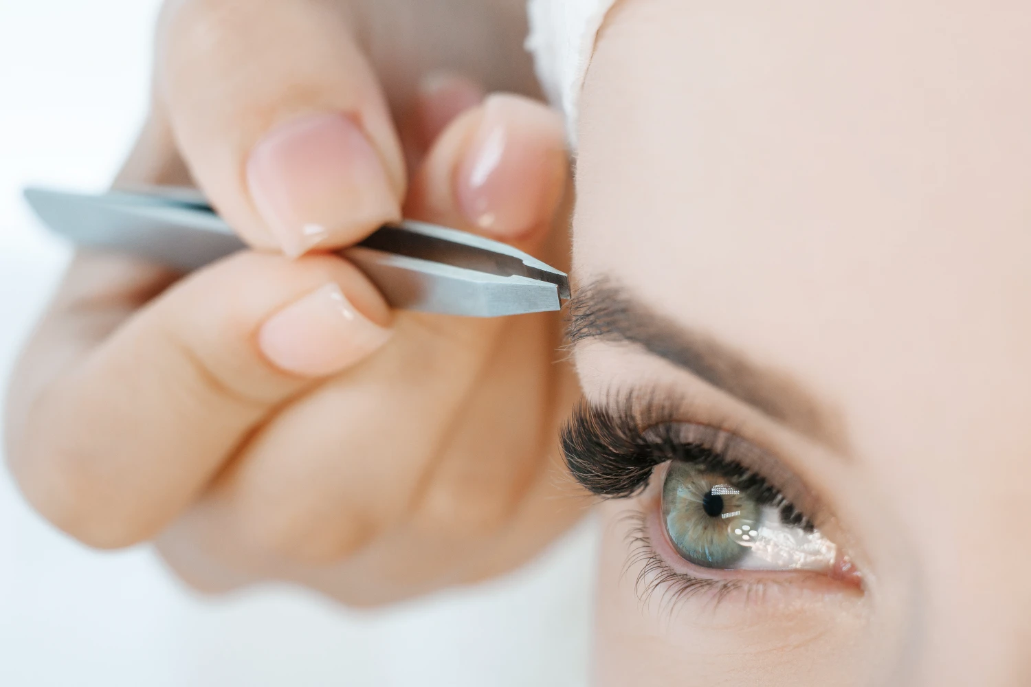 Schönes junges Mädchen mit langen Wimpern, das sich in einem Schönheitssalon die Augenbrauen zupft.